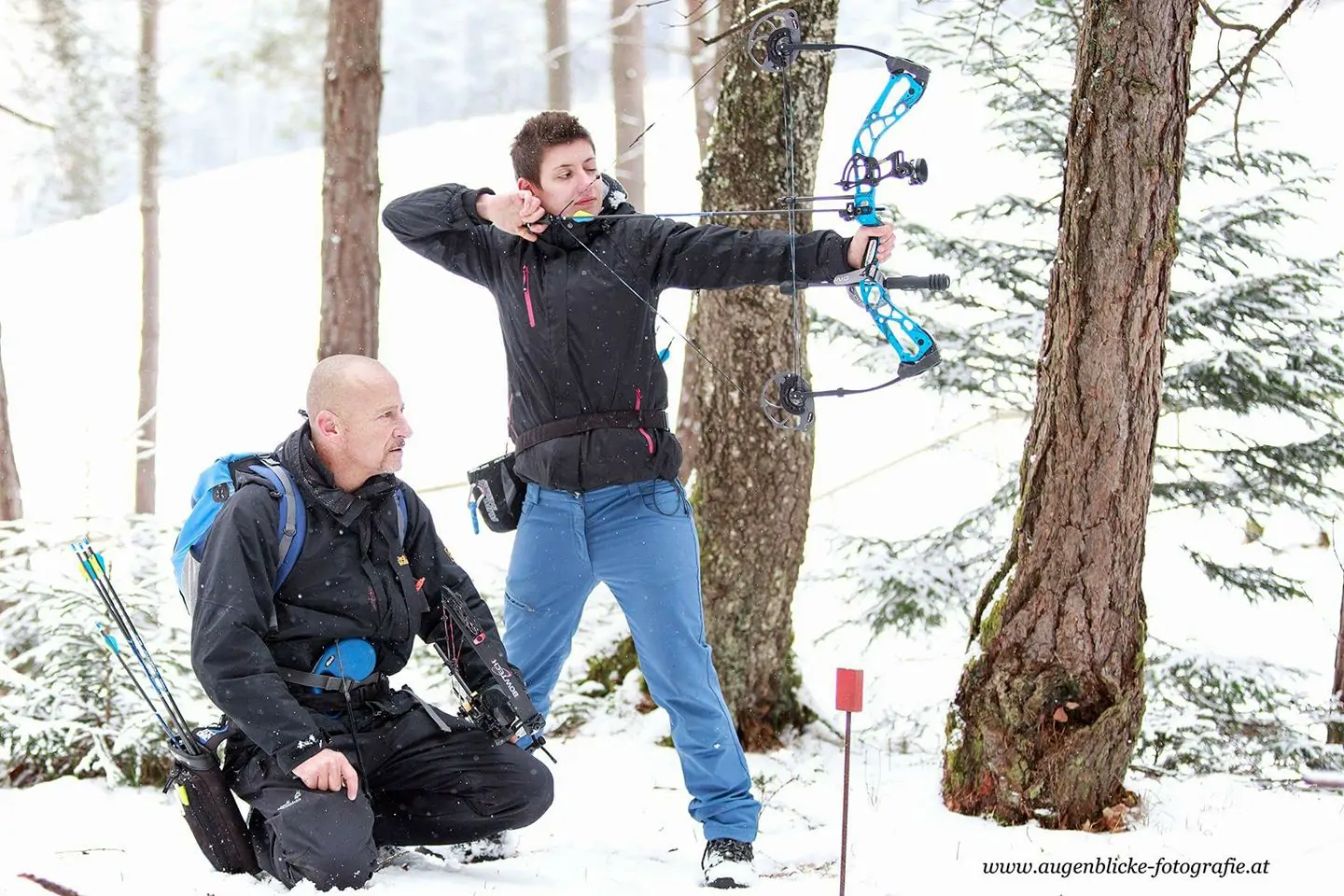Ein Bild von zwei Bogenschützen im 3D Parcours Stadlerhof. Eine männliche Person kniet auf dem Boden, während eine weibliche Person steht und mit dem Bogen zielt.