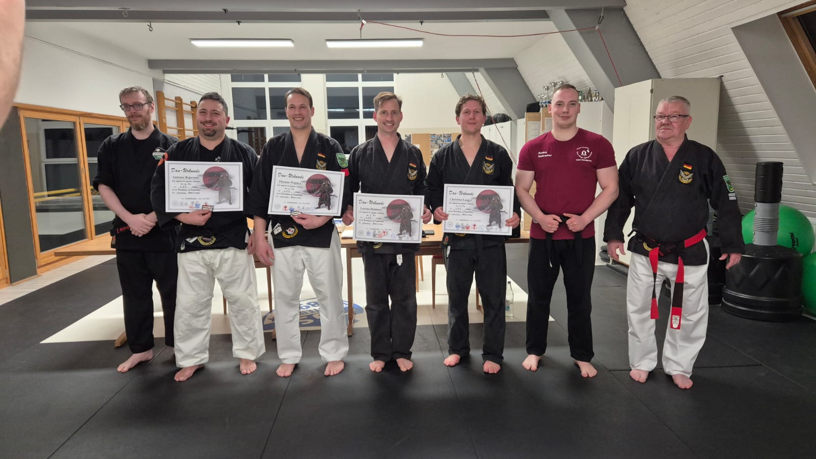 Die Prüflinge stehen nebeneinander mit den Prüfern und halten ihre Urkunden hoch.